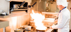 chef cooking in commercial kitchen with pan in flames