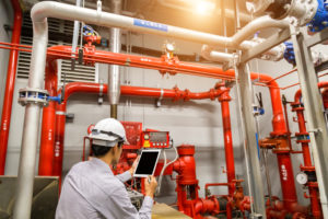 Engineer with tablet check red generator pump for water sprinkler piping and fire alarm control system.