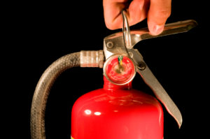 A hand pulls the pin on a red fire extinguisher