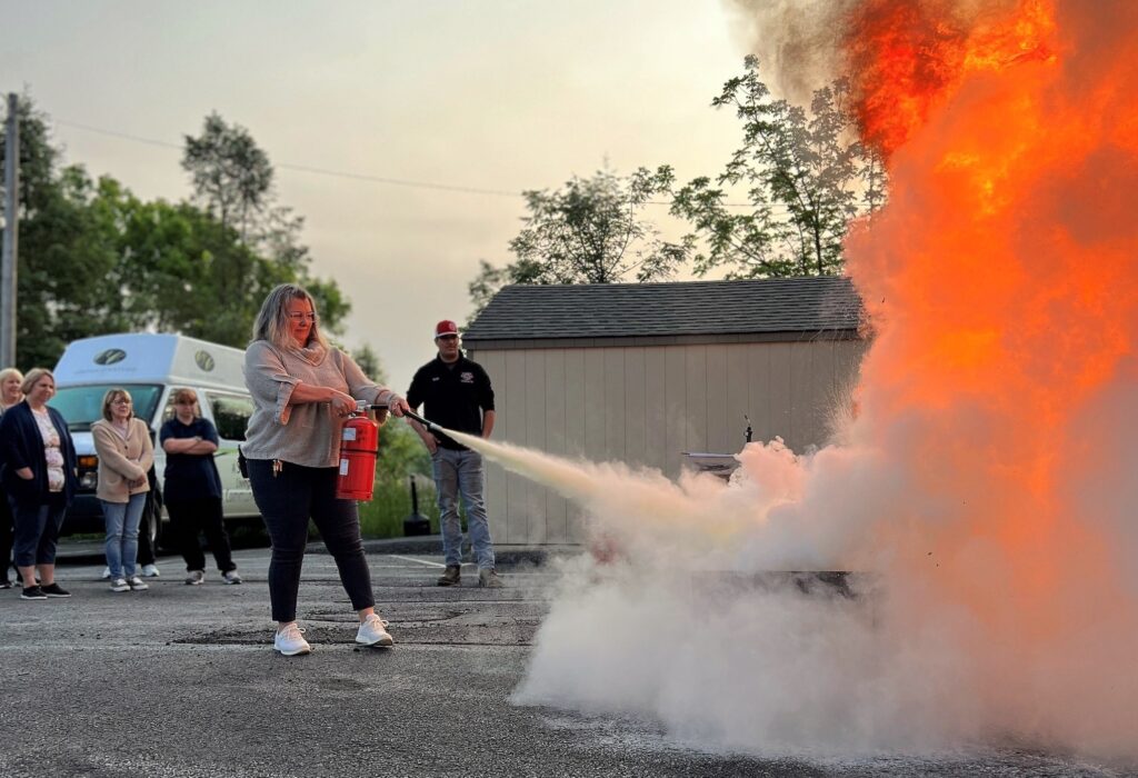 Female team member of Liberty Fire Solutions putting out a fire with a fire extinguisher.